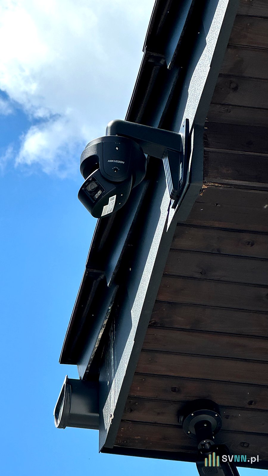 Czarna kamera Hikvision na wysięgniku ściennym pod drewnianym okapem
